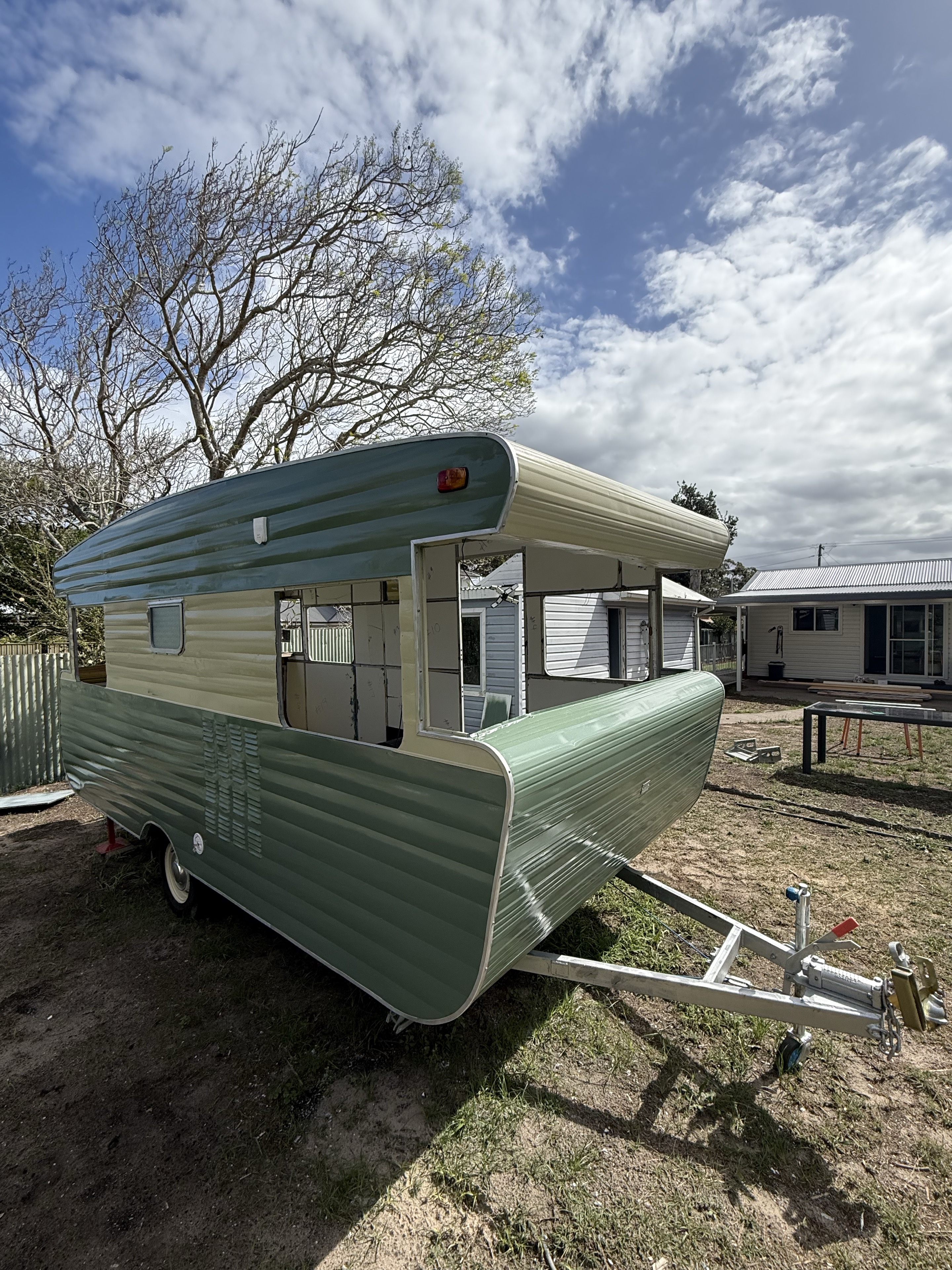 Front and side of the sage-green and cream caravan with the windows removed during restoration.